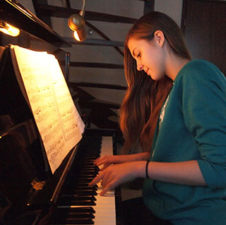 teenage girl playing piano with a smile on her face