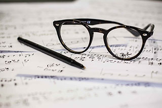 glasses and a pen resting on sheet music