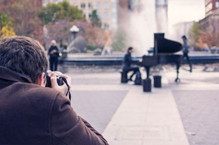 man photographing a man playing a grand piano in the middle of park by fountain