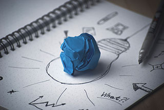 sketch of a light bulb with doodles drawn around it a wad of blue paper on top